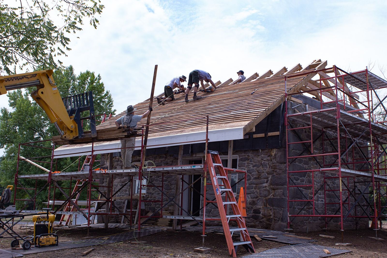 Cedar shingles lifted onto a roof by telehandler while the crew works at the ridge