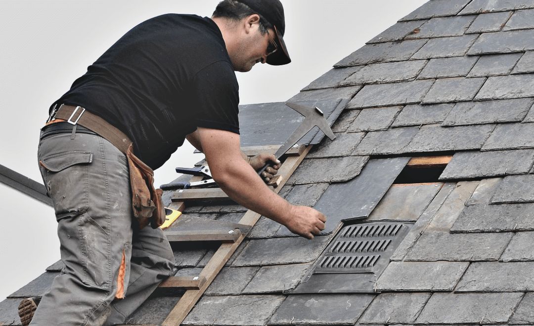 Roofer replacing damaged slates on a pitched roof